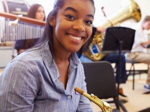 Smiling female high school pupil with saxophone