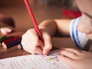 Little girl writing in an activity book. Representing Exploring the National Standard of Writing at Greater Depth within the Expected Standard (GDS) at End of KS2