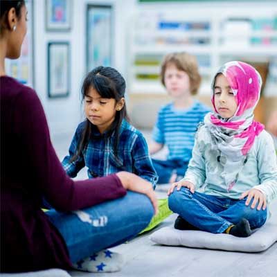 Picture of three pupils and a teacher sat cross legged with eyes closed in a classroom, meditating, represents an emotionally safe classroom